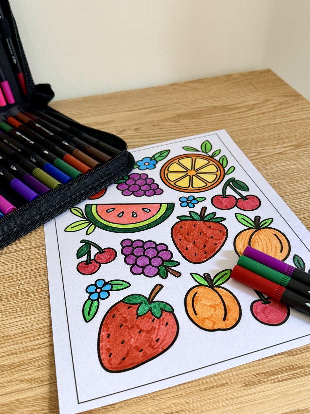 Lámina de frutas coloreada junto al estuche de marcadores BRILL